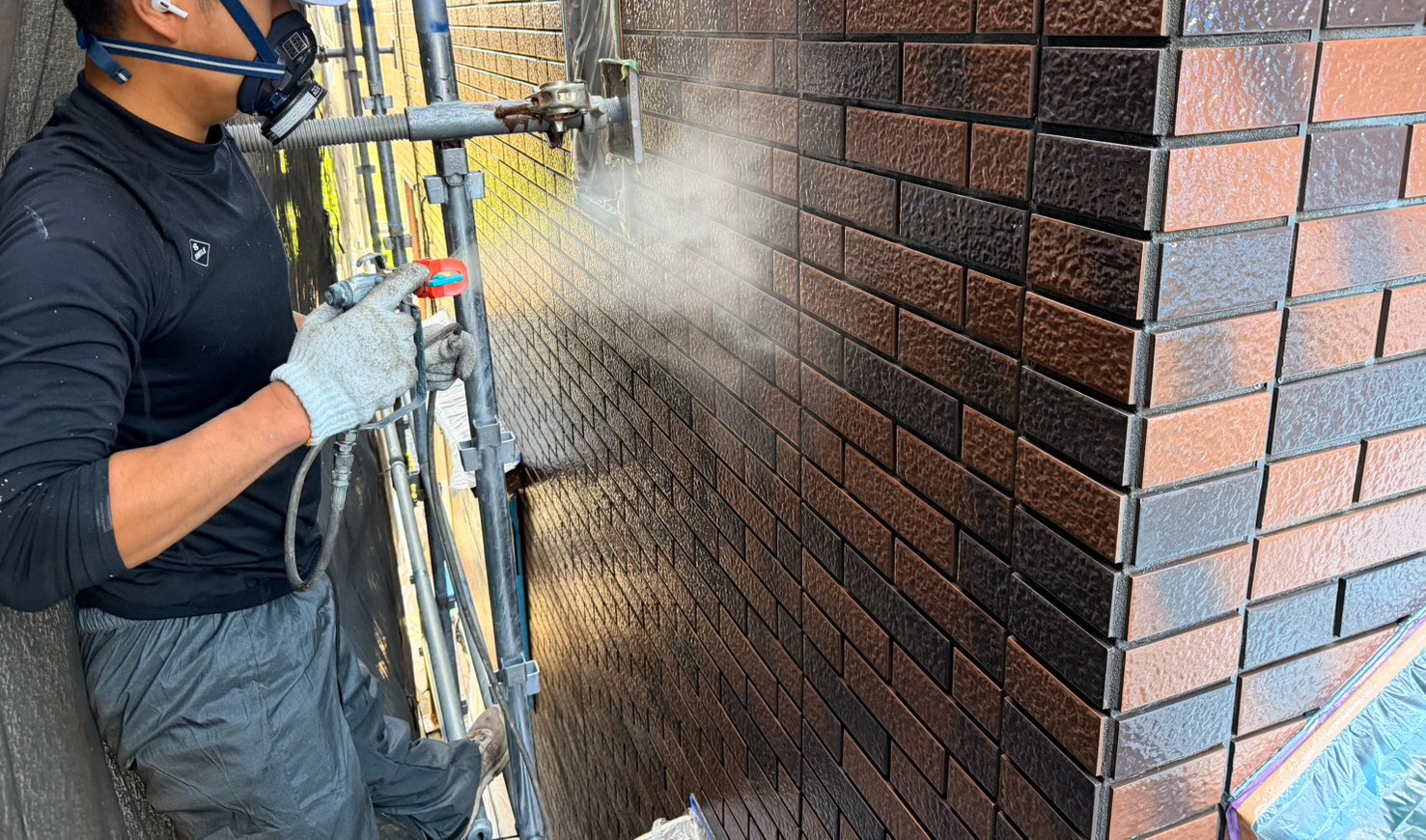 凹凸の深いタイルにクリヤー塗料をエアレスで吹き付けている様子｜深目地タイルへの均一なクリヤー塗装作業